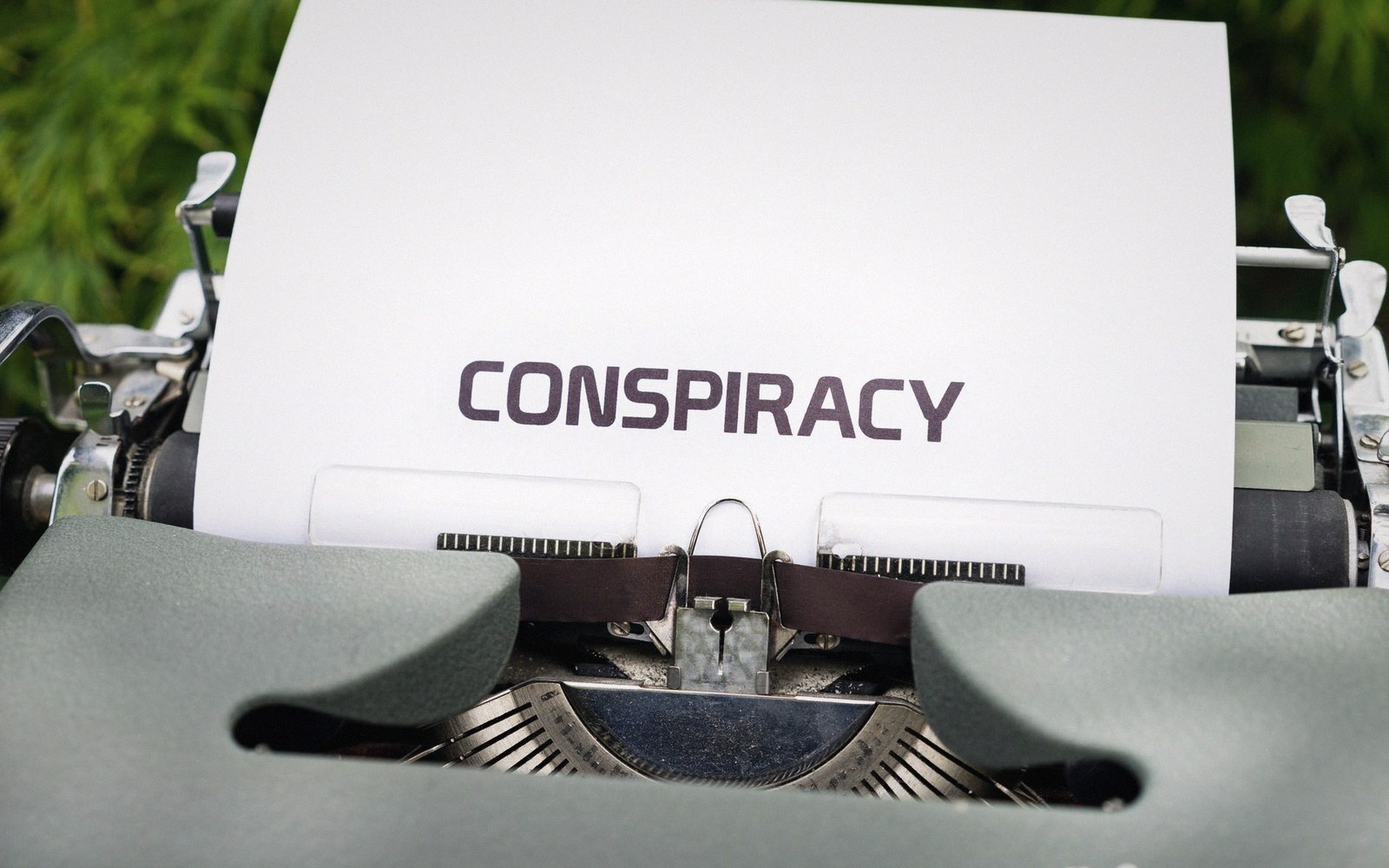 A vintage typewriter with a sheet of paper reading "conspiracy" rolled into it