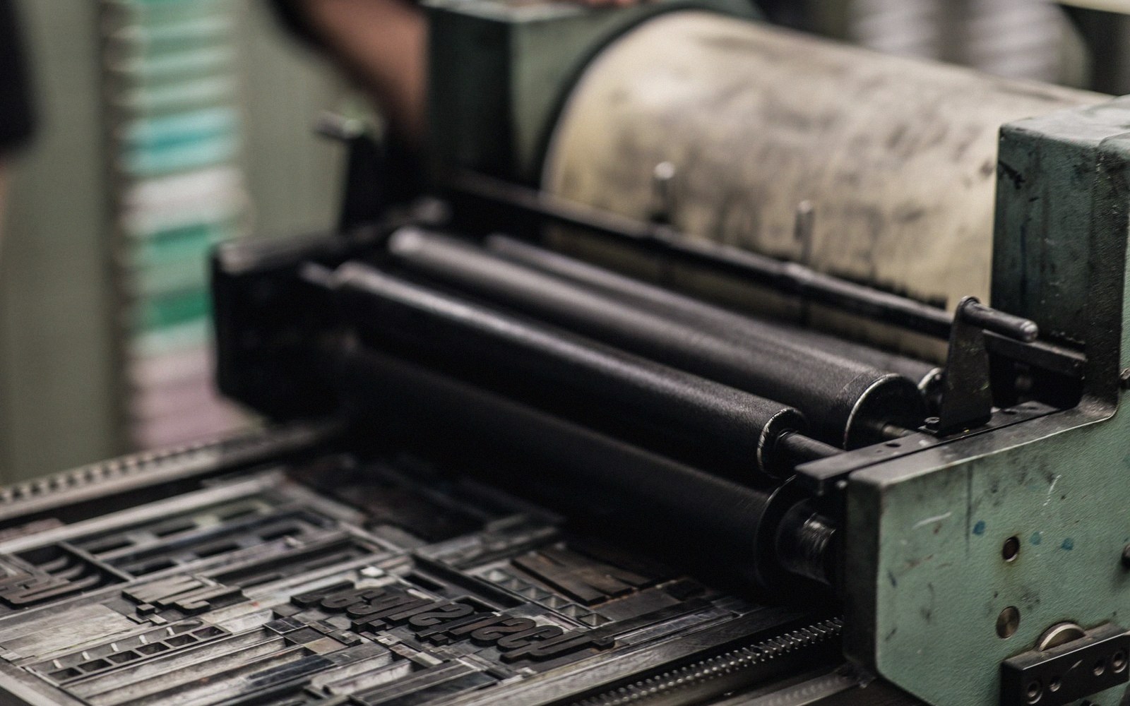 Inked rollers on a letterpress printing machine above metal type set in a chase