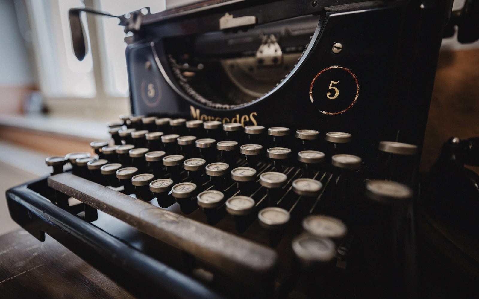 Close-up of a vintage black Mercedes typewriter with round keys on a wooden desk