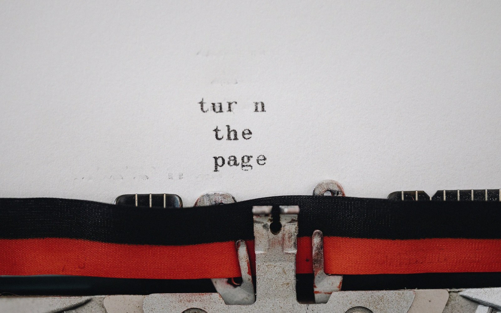 Typewriter paper reads "turn the page" above the black and red ink ribbon